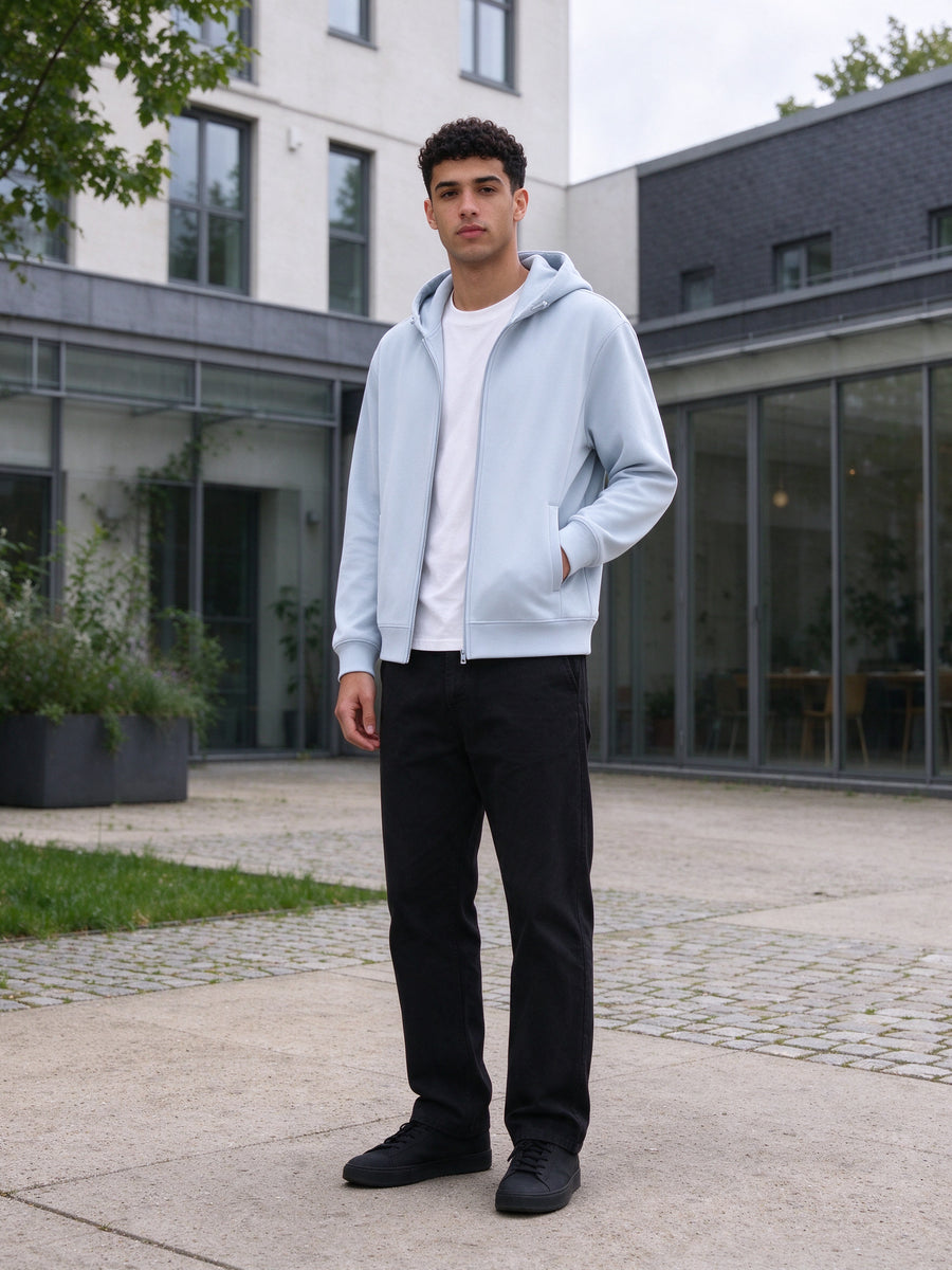 Marcel Afters Regular Fit Full Zip Hoodie in Light Blue, worn by a man, in a modern Copenhagen courtyard in a light blue regular-fit full-zip hoodie over a white tee