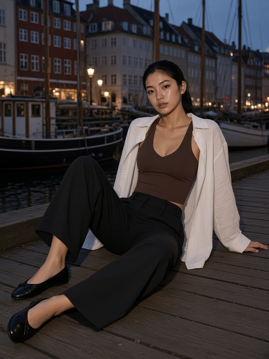 Woman in the Women's V-Neck Yoga Sports Bra in Coffee under an open linen shirt on Nyhavn quay in Copenhagen at dusk