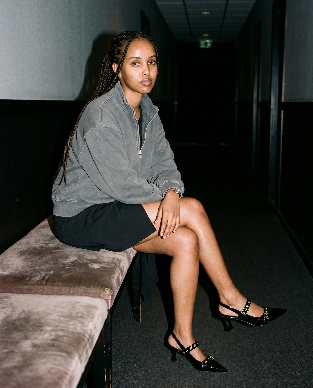 Woman in Gray vintage wash fleece quarter-zip sweatshirt and a black skirt, seated in a dark hallway