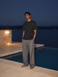 Marcel Afters Vintage Wash Paneling T-Shirt in Black, worn by a man, standing barefoot on an infinity-pool ledge at dusk