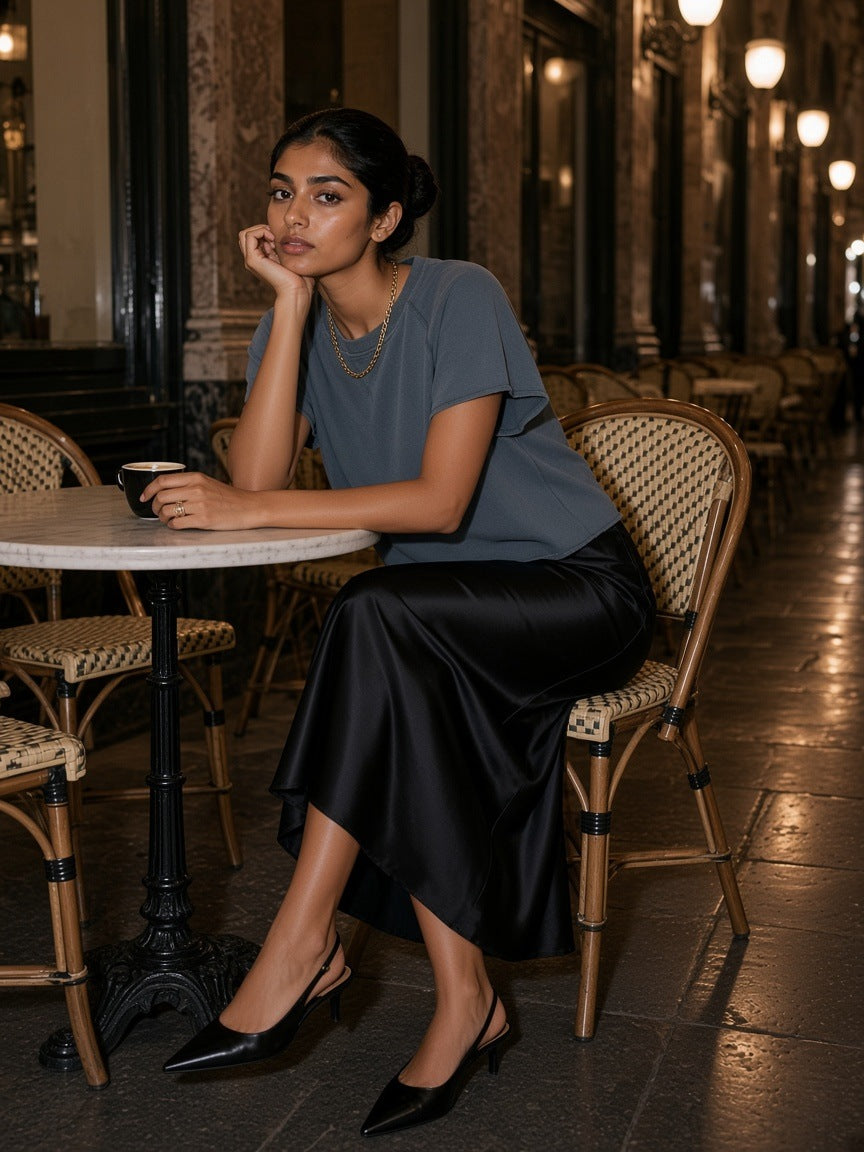 Woman in the Vintage Wash Raw Edge Boxy T-Shirt in Gray Blue at a marble café table in a glass-roofed Brussels arcade at night