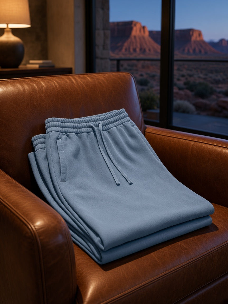Marcel Afters Vintage Wash Sweatpants in Jeans Blue, laid flat, leather armchair