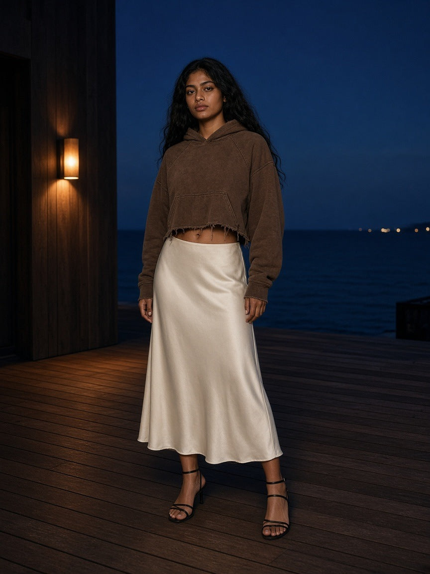 Marcel Afters Vintage Washed Frayed-Hem Hoodie in Brown, worn by a woman, standing on a lit deck by the sea in a satin skirt