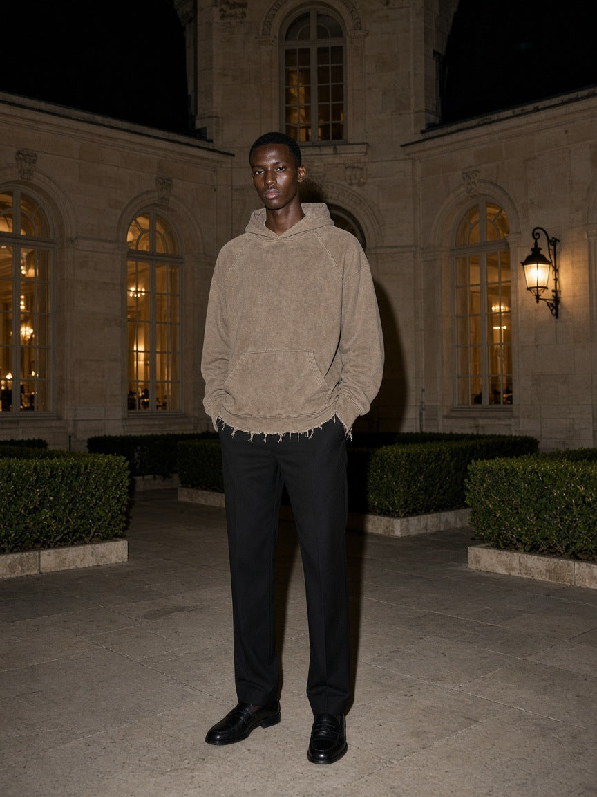 Marcel Afters Vintage Washed Frayed-Hem Hoodie in Gray Camel, worn by a man, standing in a floodlit palace courtyard at night