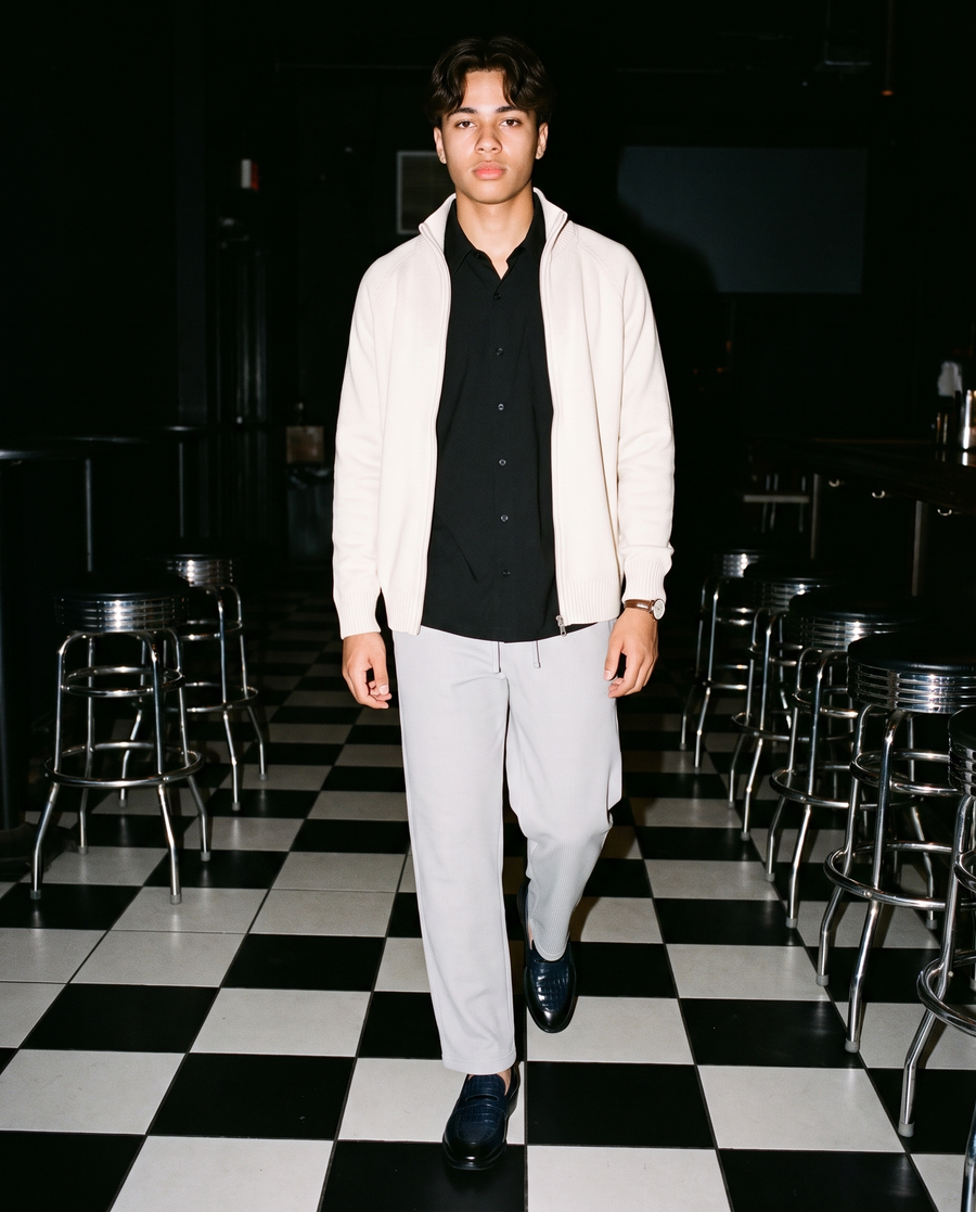 Man in Light Gray waffle barrel leg pants with a cream zip jacket and a black shirt, on a checkered floor