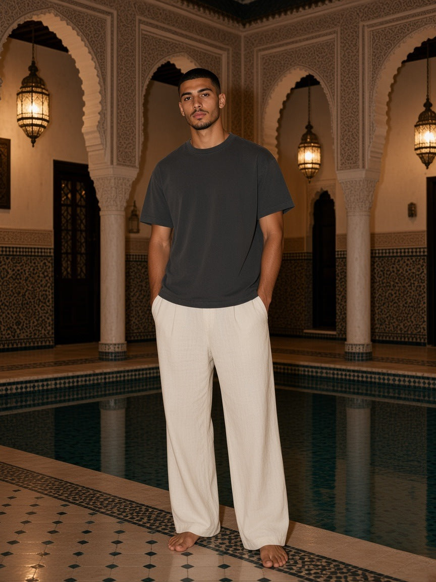 Marcel Afters Washed Rolled Hem Half Sleeve T-Shirt in Dark Gray, worn by a man, standing in an arched palace courtyard by the pool