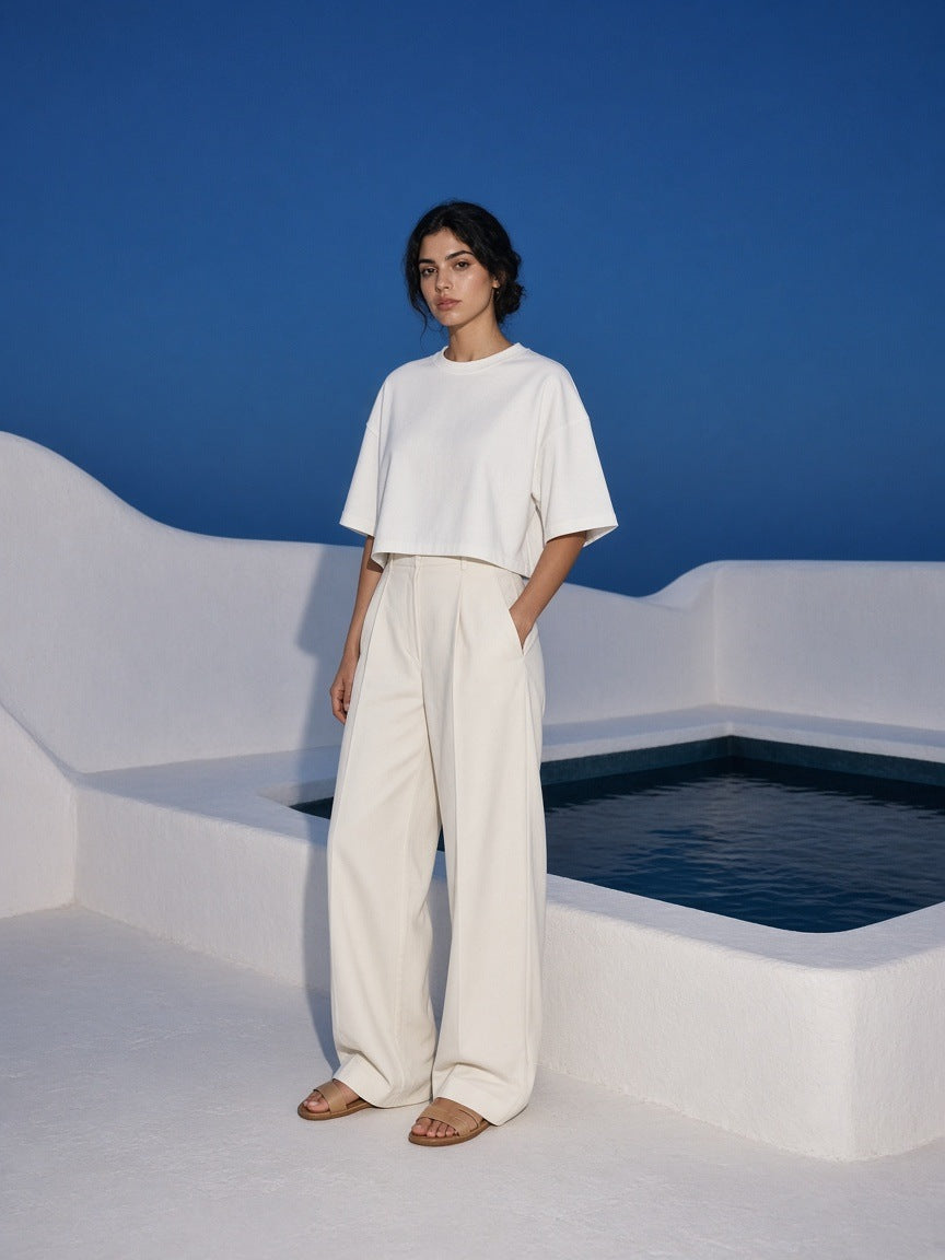 Marcel Afters Women's Heavyweight Boxy T-Shirt in White, worn by a woman, standing by a white plunge pool in a cropped tee and wide trousers
