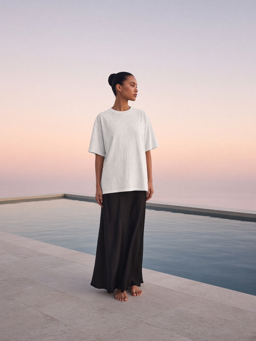 Marcel Afters Women's Heavyweight Mineral Wash Boxy T-Shirt in White, worn by a woman, standing on a stone terrace at sunset in a long black skirt