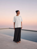 Marcel Afters Women's Heavyweight Mineral Wash Boxy T-Shirt in White, worn by a woman, standing on a stone terrace at sunset in a long black skirt