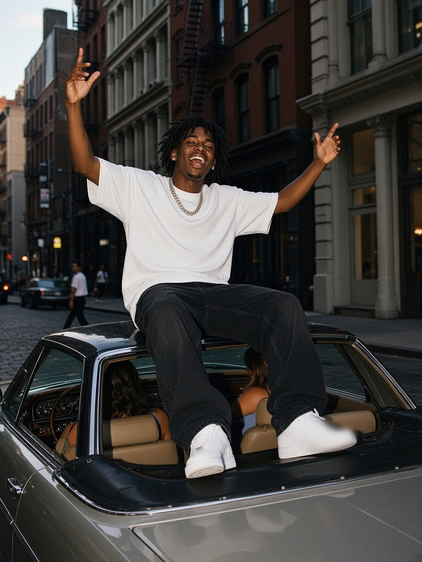 Man in the Men's Boxy Oversized T-Shirt in White with black jeans, sitting up on a vintage convertible on a SoHo street in New York at dusk