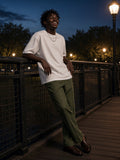 Man in the Men's Boxy Oversized T-Shirt in White leaning on the railing of a Brooklyn Bridge Park pier at night