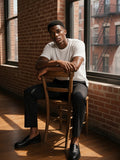 Man in the Essential Heavyweight Cotton T-Shirt in White leaning by a loft window in Tribeca, New York in the morning