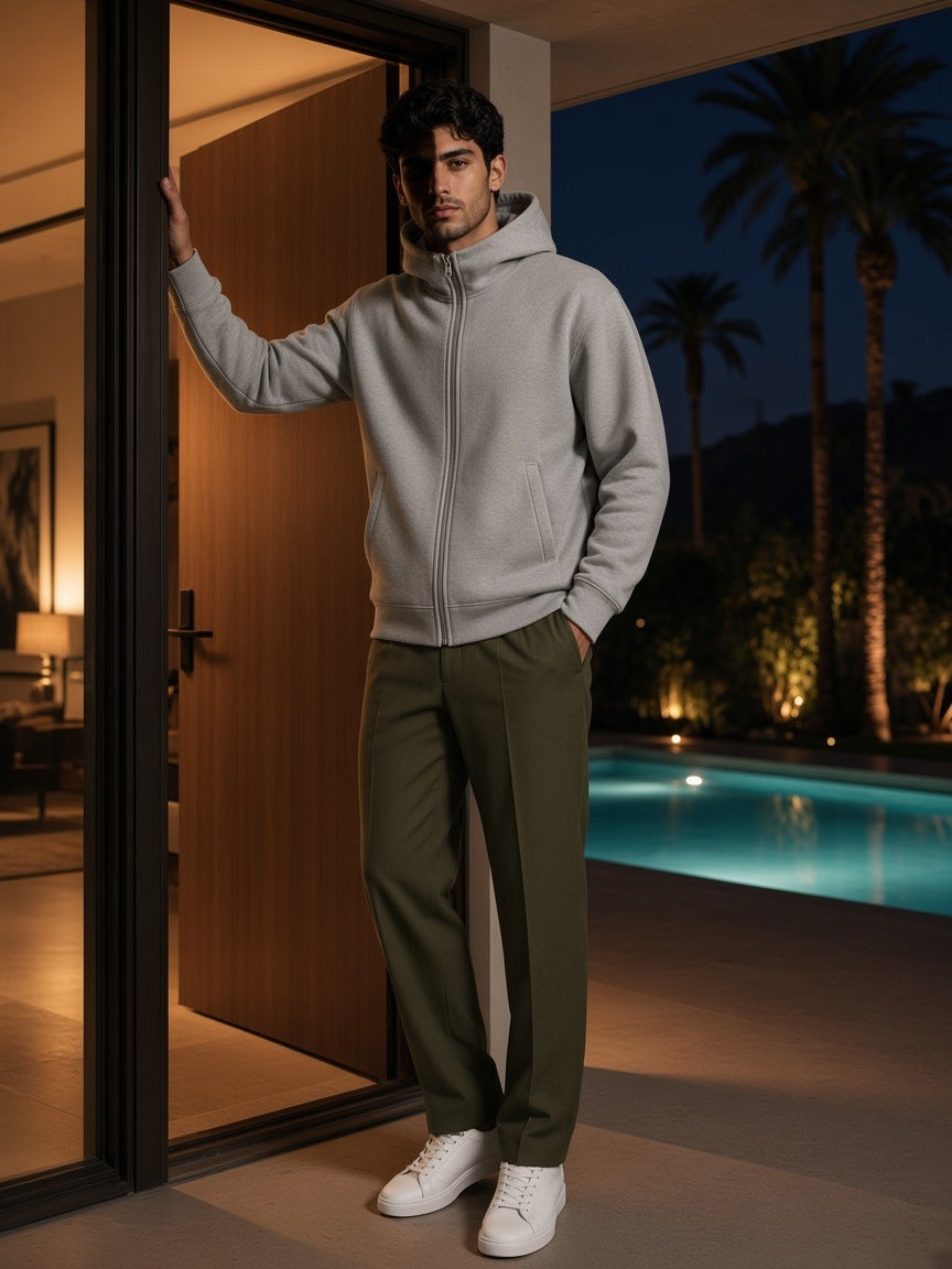 Man in the Men's Essential Heavyweight High Neck Zip-Up Hoodie in Flower Gray with olive wool trousers and white sneakers, in the doorway of a mid-century house by a lit pool in Palm Springs at night