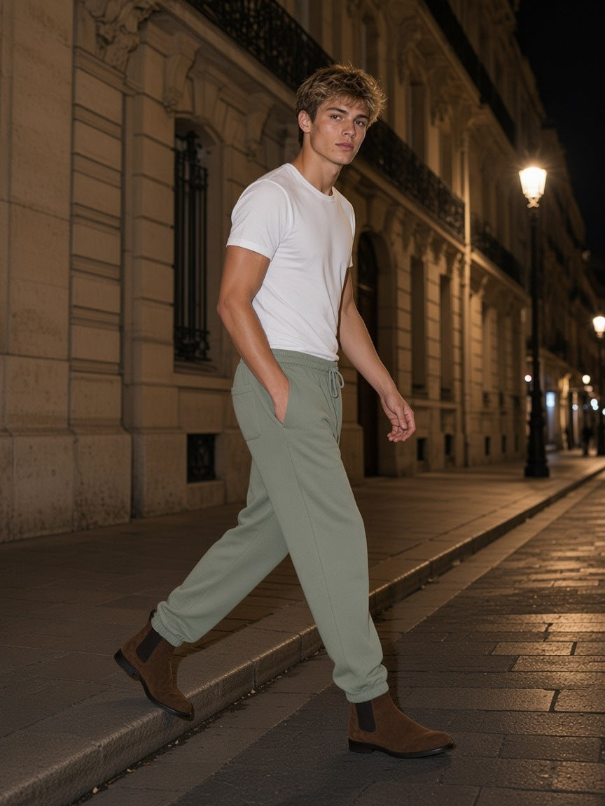 Man in the Men's Heavyweight Fleece Joggers in Grayish Green stepping off a kerb on a Haussmann boulevard in Paris at night