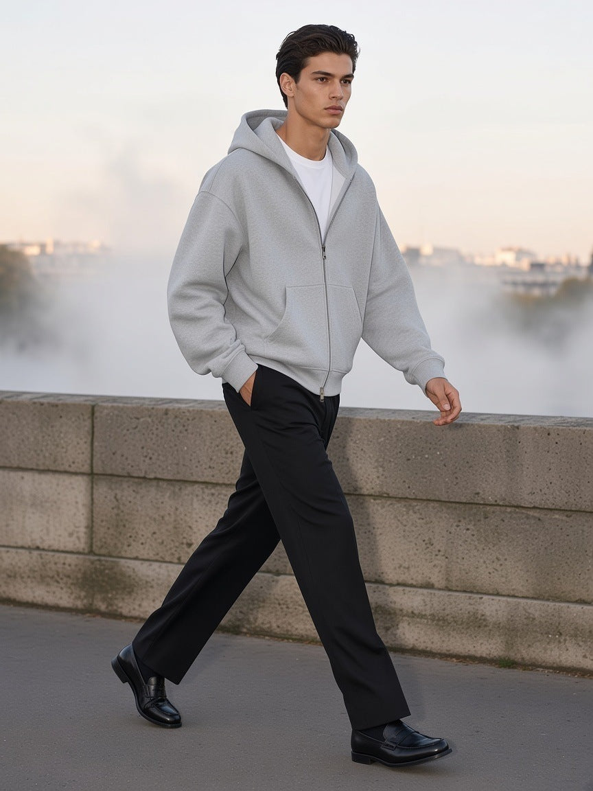 Man in the Men's Heavyweight Full Zip Boxy Hoodie in Flower Gray with black trousers, walking along a stone quai in Paris at dawn