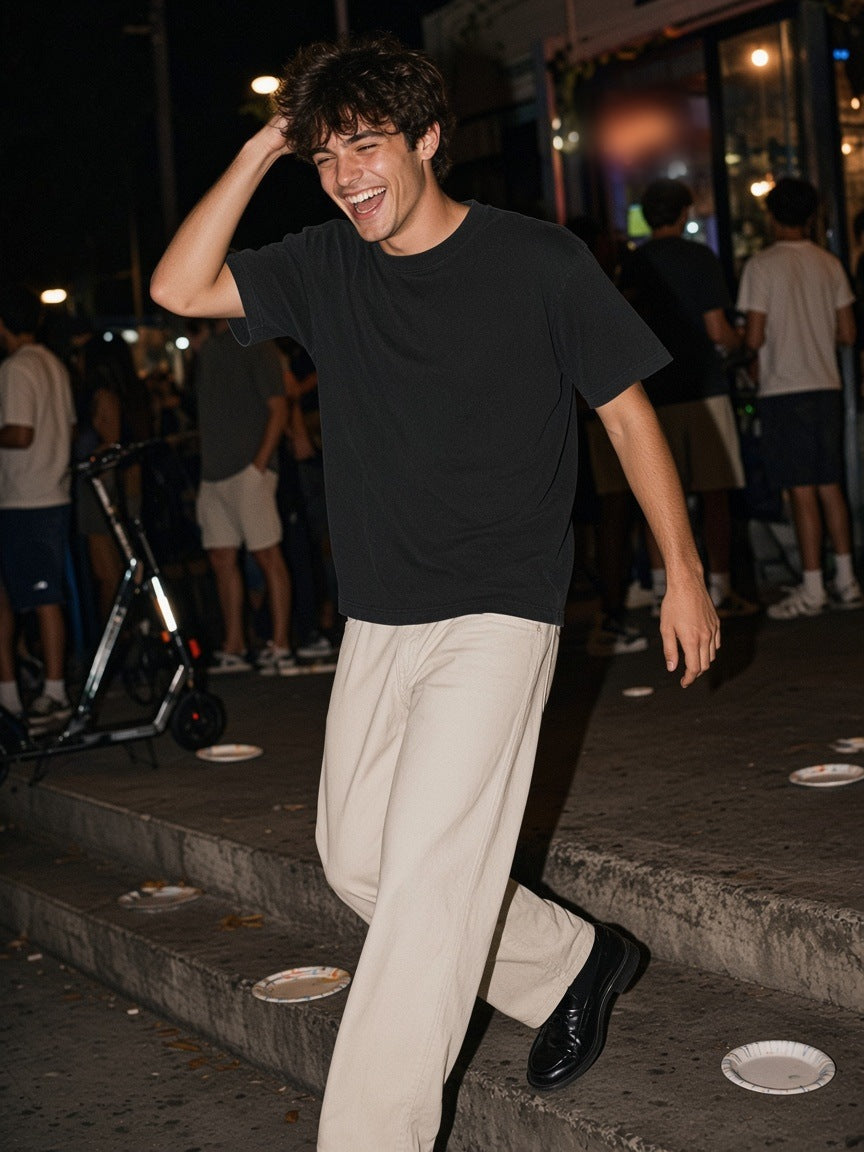 Man in the Men's Heavyweight Vintage Washed Frayed T-Shirt in Black with stone trousers and loafers, laughing down the steps outside a late-night taco stand in Silver Lake, Los Angeles