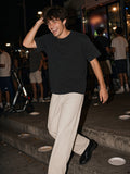 Man in the Men's Heavyweight Vintage Washed Frayed T-Shirt in Black with stone trousers and loafers, laughing down the steps outside a late-night taco stand in Silver Lake, Los Angeles