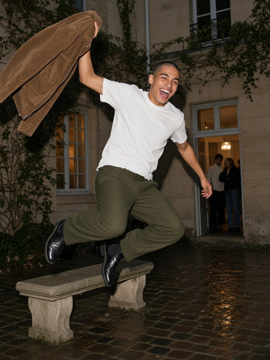 Man in the Men's Heavyweight Vintage Washed Frayed T-Shirt in White with olive trousers, leaping off a bench in a Paris courtyard at night