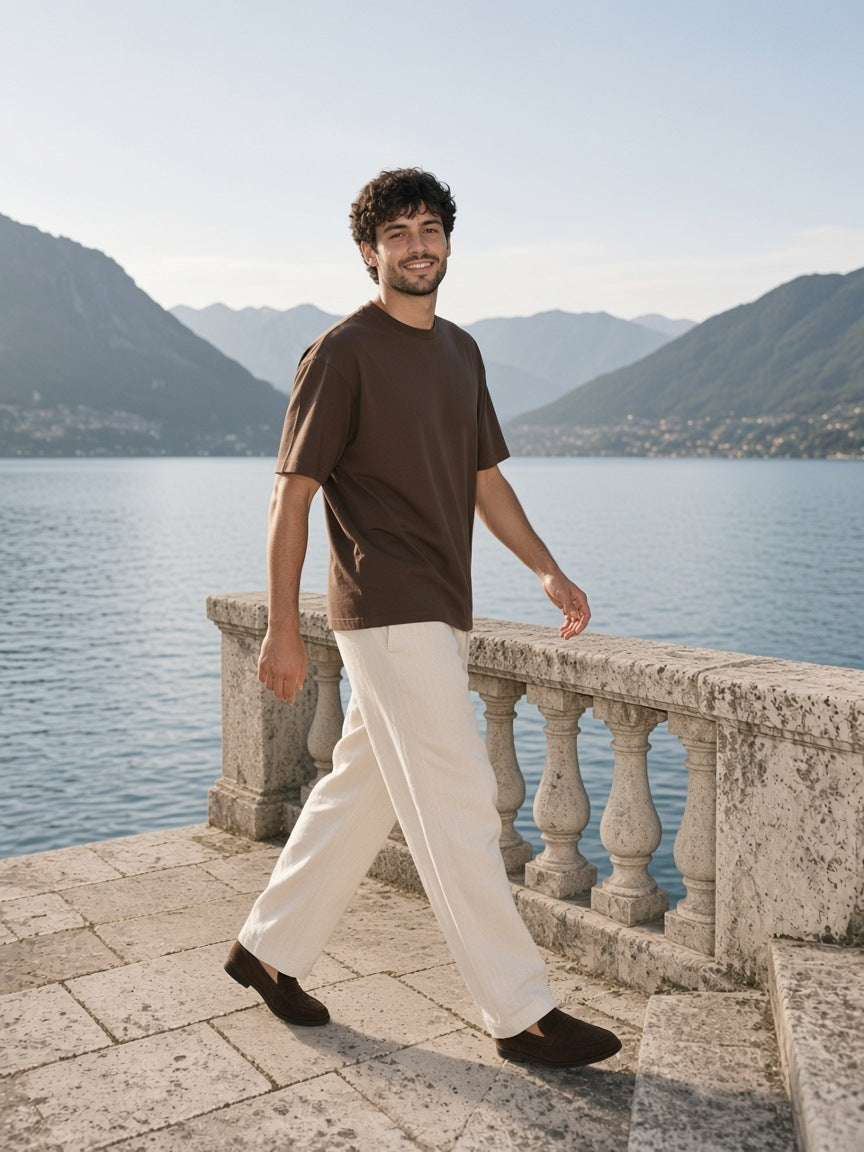 Man in the Men's Oversized T-Shirt in Coffee sitting on a villa dock balustrade on Lake Como by day