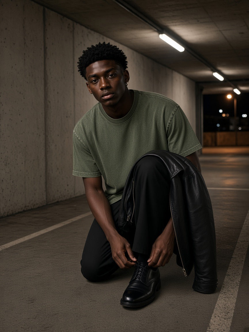 Man in the Men's Snow Washed Heavyweight Oversize T-Shirt in Green tying his shoe on a Berlin car park ramp at night