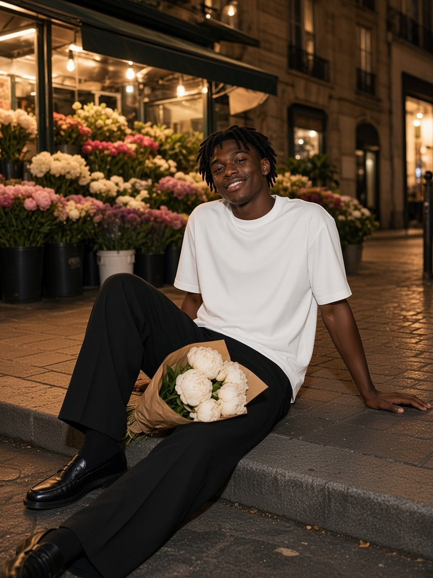 Man in the Men's Heavyweight Drop Shoulder T-Shirt in White with peonies on the steps of a Paris flower kiosk at night