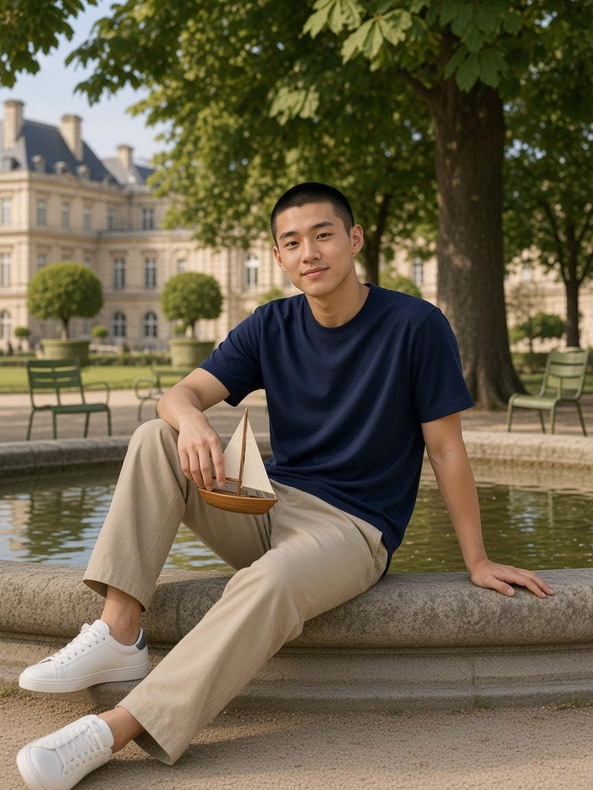 Man in the Men's Heavyweight Earth Tone T-Shirt in Navy on the rim of the basin in the Jardin du Luxembourg
