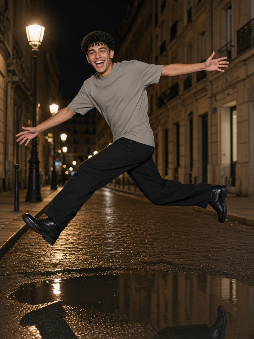Man in the Men's Heavyweight Earth Tone T-Shirt in Gray Camel leaping a puddle on a cobbled Paris street at night