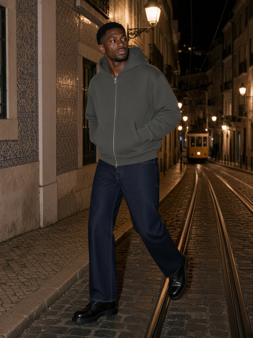 Man in the Men's Heavyweight Full Zip Boxy Hoodie in Dark Gray with raw indigo jeans and black leather boots, stepping off a kerb onto tram rails in Lisbon's Bairro Alto at night