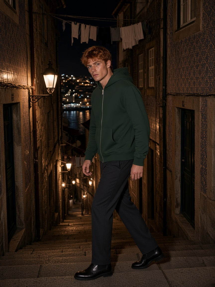 Man in the Men's Heavyweight Full Zip Hoodie in Blackish Green with charcoal trousers and black Chelsea boots, climbing a stone stairway in Porto's Ribeira at night