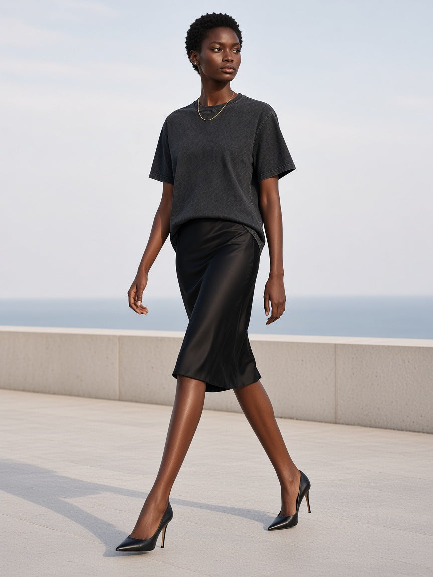 Woman in the Marcel Afters Mineral Wash Boxy Cotton T-Shirt in Black, on a pale stone terrace above the sea in Mykonos