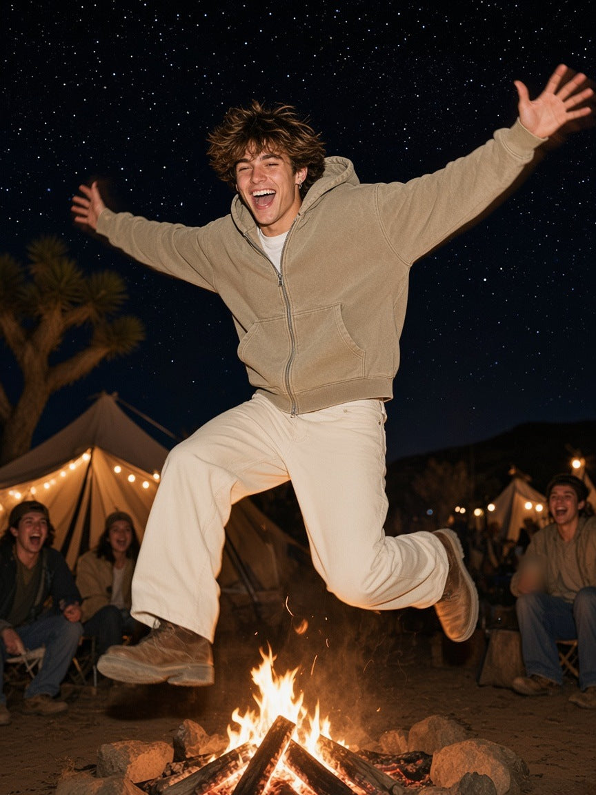 Marcel Afters Mineral Wash Boxy Full Zip Hoodie in Khaki, worn by a man, leaping over a night campfire in a khaki boxy zip hoodie under the stars