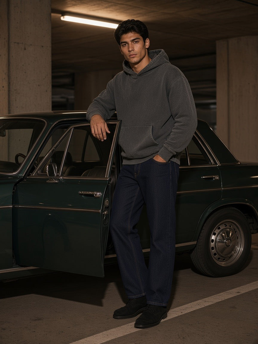 Man in the Mineral Wash Boxy Hoodie in Dark Gray with indigo jeans beside a vintage car in a car park at night