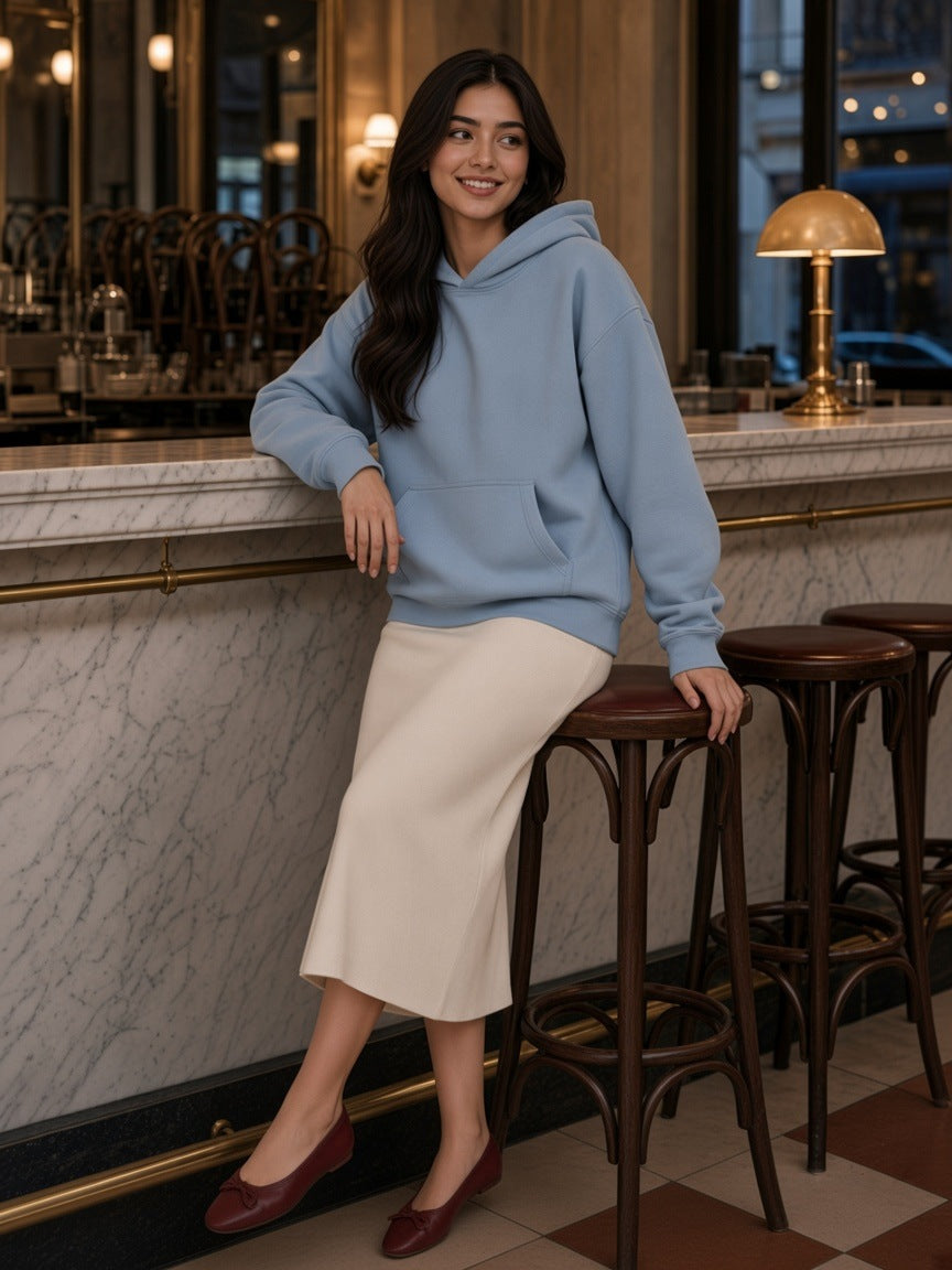 Woman in the Mineral Wash Boxy Hoodie in Haze Blue with an ivory knit midi skirt at the marble bar of a Viennese cafe