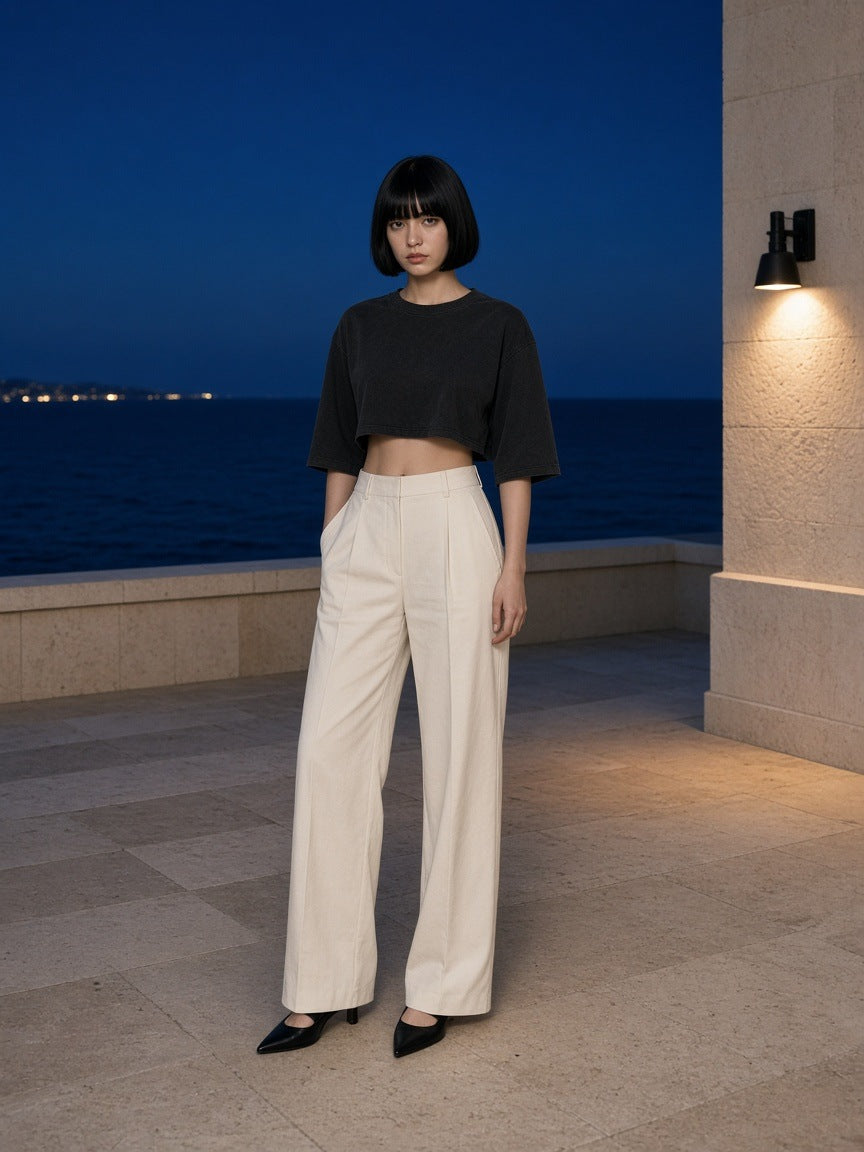 Woman in the Mineral Wash Raw Hem Boxy T-Shirt in Black with ivory wide trousers on a clifftop resort terrace in Sydney at blue hour