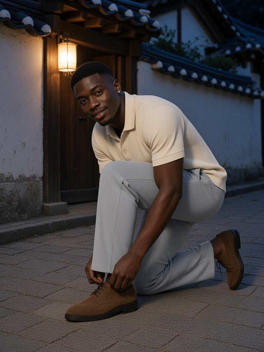 Man in the Mineral Wash Straight Sweatpants in Light Gray with a cream knit polo and suede derbies, kneeling to tie a shoe in a Bukchon hanok lane in Seoul at night