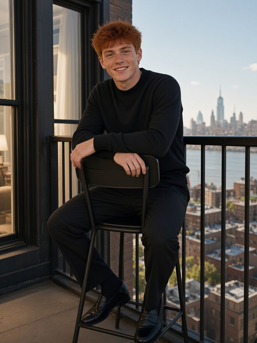 Man in the Mock Neck Sweatshirt in Black, perched on a chair on a loft balcony in Tribeca, New York in the morning