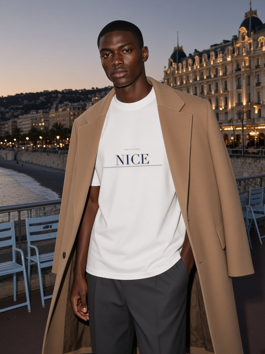 Man in the Nice Heavyweight Drop Shoulder T-Shirt in White with the navy Nice city plate, on the seafront promenade in Nice at dusk