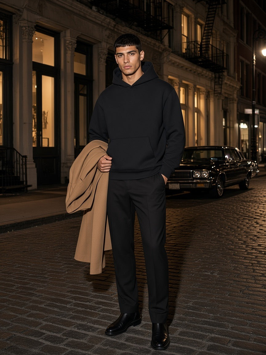 Man in the Marcel Afters Oversize Heavyweight Fleece Hoodie in Black Beauty on a cobbled SoHo street in New York at night
