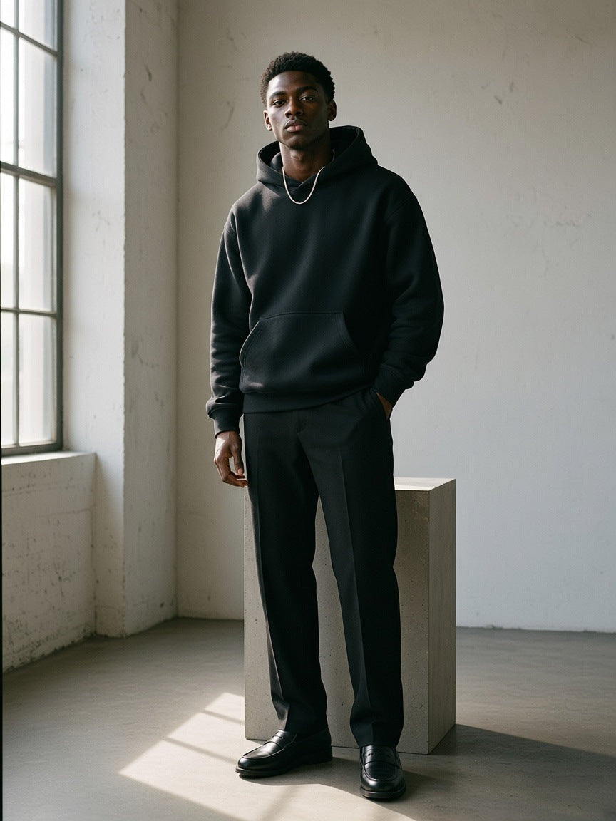 Man in the Oversize Heavyweight Fleece Hoodie in Black Beauty by a stone plinth in a daylit concrete studio in the morning