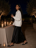 Woman in the Oversized Collared Sweatshirt in Oat Gray with a black satin skirt, raising a glass on a candlelit vineyard terrace at night