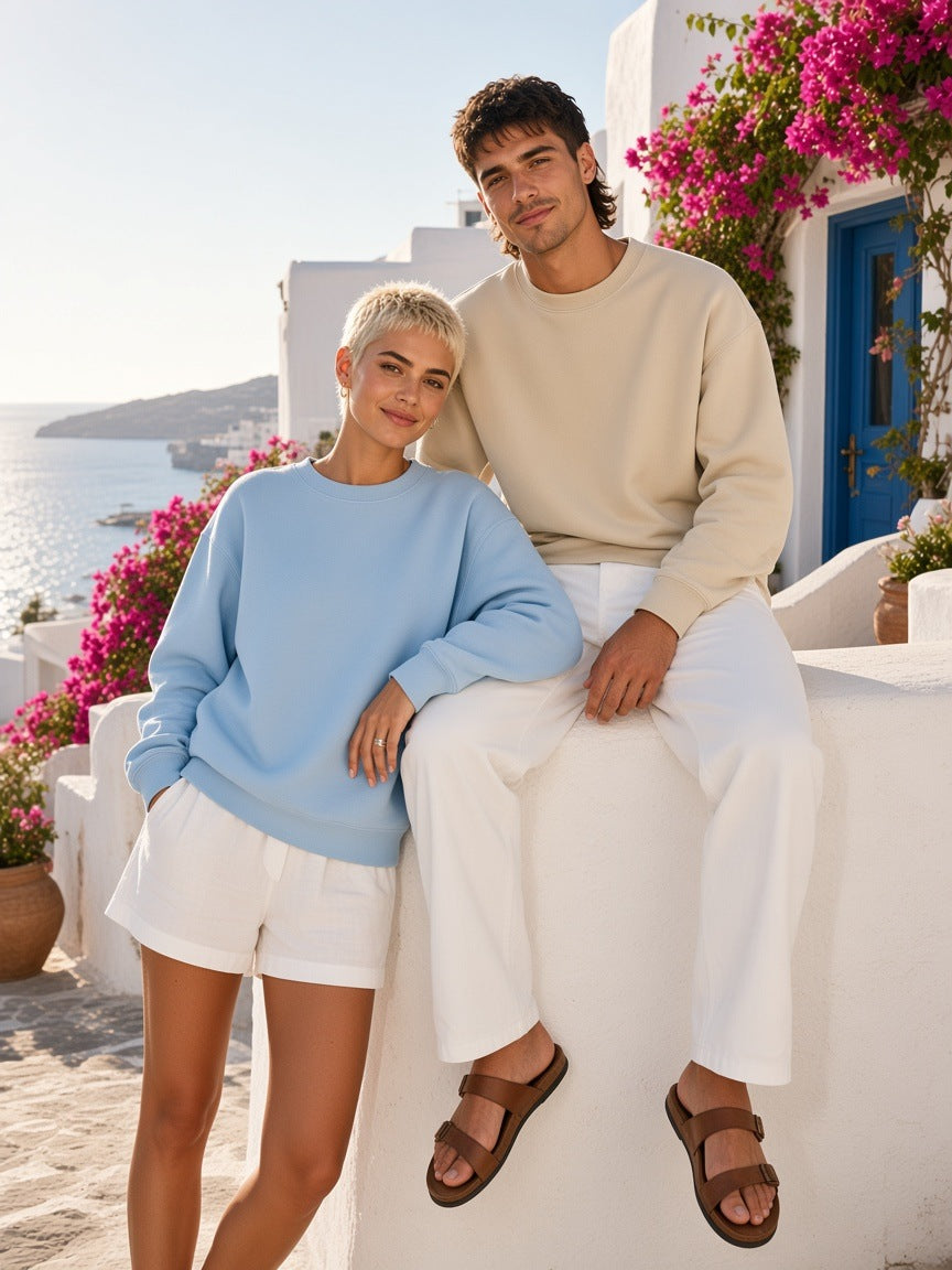 Marcel Afters Oversized Crewneck Sweatshirt in Light Blue, worn by a man and a woman, sitting together on a whitewashed wall under bougainvillea, she in light blue and he in camel