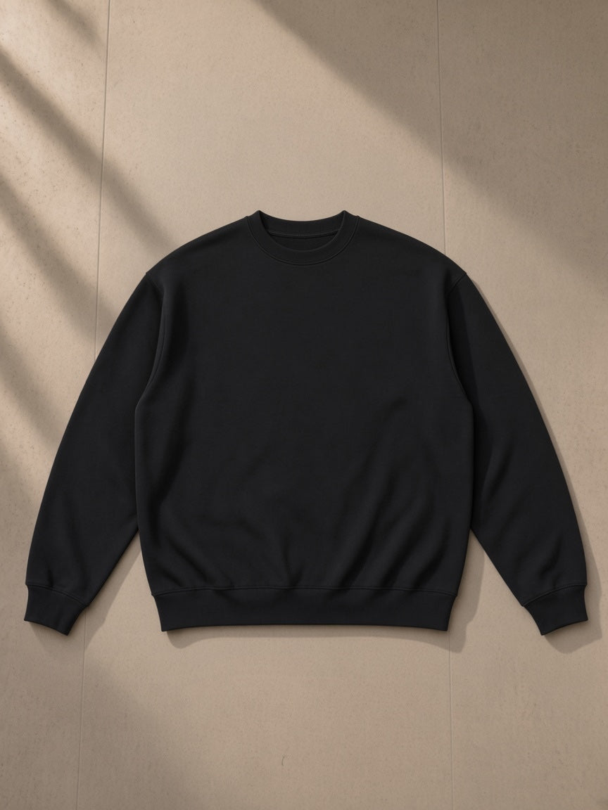 Oversized drop shoulder crewneck sweatshirt in Black, laid flat on pale limestone, front view