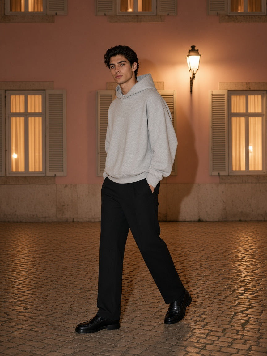 Man in the Marcel Afters Oversized Drop Shoulder Hoodie in Flower Gray with black trousers and loafers, walking past a rose stucco wall under a streetlamp at night
