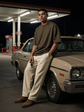 Man in the Oversized Drop Shoulder T-Shirt in Brown leaning on a vintage car at a desert gas station at night