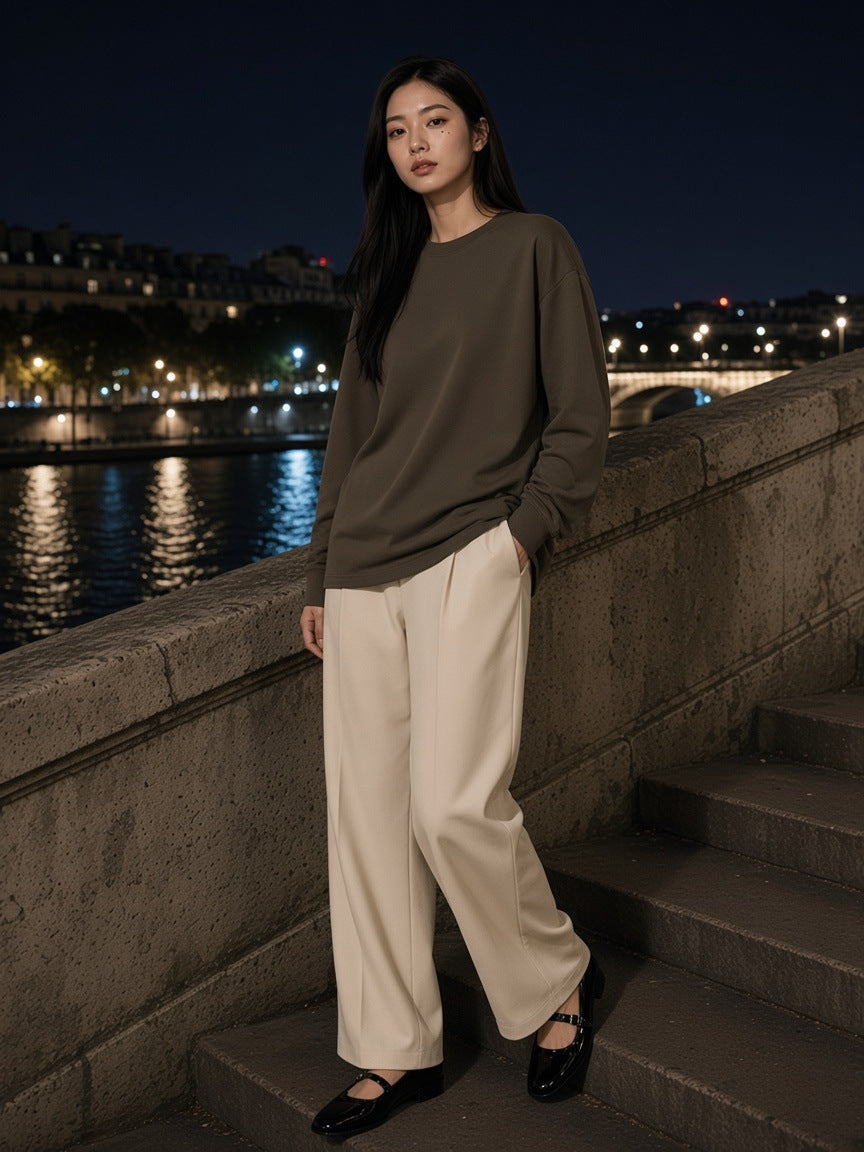 Woman in the Oversized Long Sleeve T-Shirt in Brown with ecru wide trousers and patent Mary Janes, on the Seine steps in Paris at night