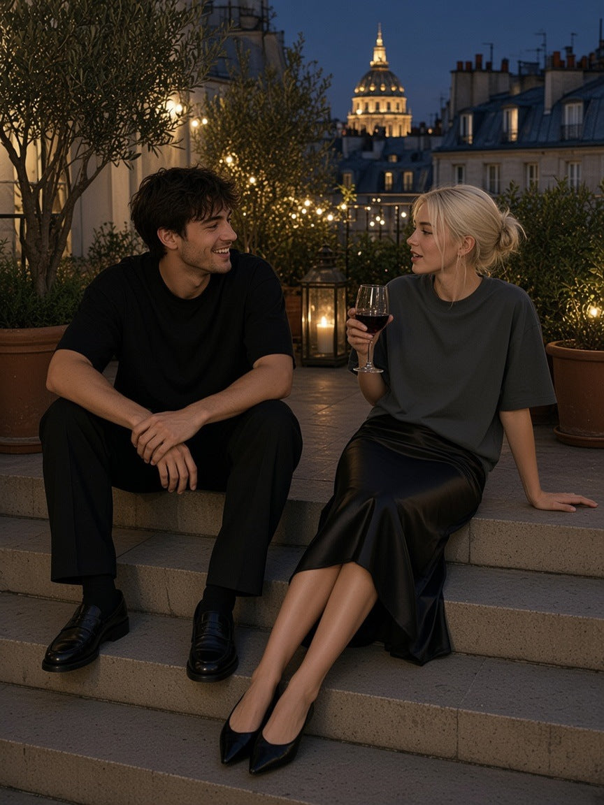 Man and woman in the Oversized One-Piece Boxy T-Shirt in Black and Dark Gray seated on a Paris rooftop terrace step at night