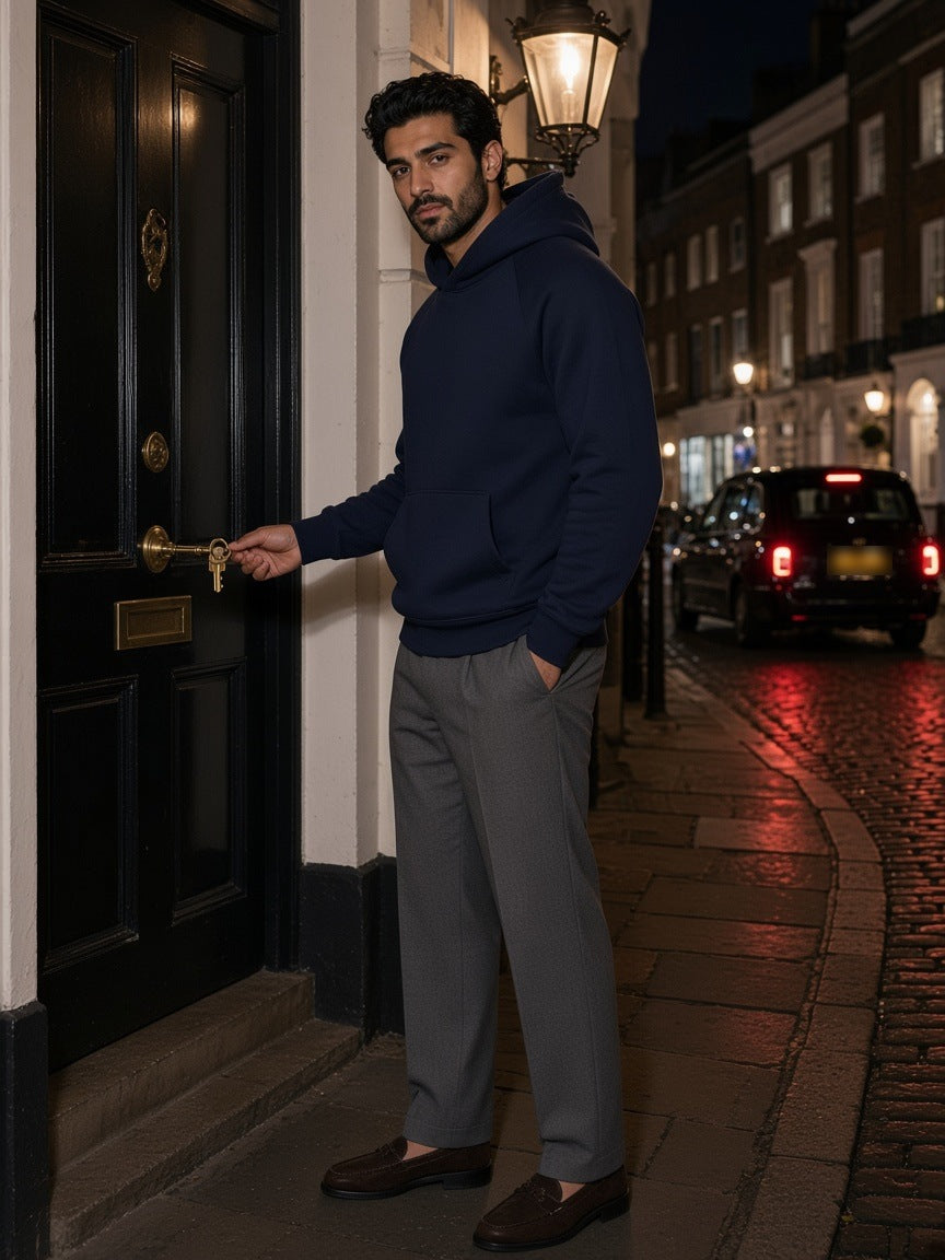 Man in the Oversized Raglan Pullover Hoodie in Navy Blue with grey flannel trousers and tassel loafers, unlocking a mews door in Soho, London at night