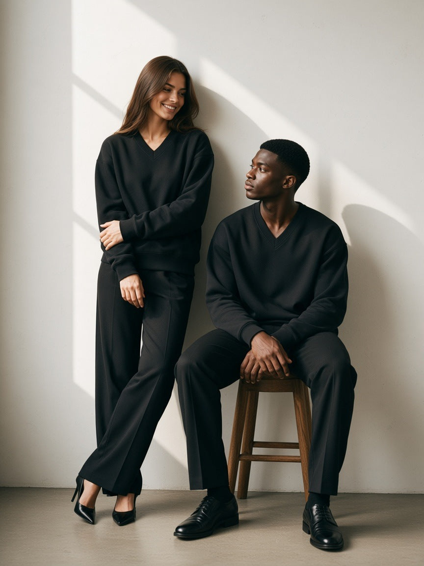 Two people in the Oversized V-Neck Sweatshirt in Black, a woman striding in heels, a man standing still, charcoal studio in the morning