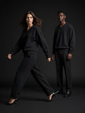 Two people in the Oversized V-Neck Sweatshirt in Black, a woman striding in heels, a man standing still, charcoal studio
