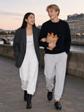 Two people in the Heavyweight Fleece Joggers in White and Flower Gray walking a Seine quai at dawn with croissants